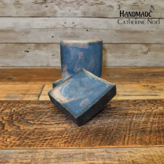 Blueberry Delight handmade Hand & Body Soap with rich blue swirls accented by earthy brown tones, placed on a rustic wooden surface, created by Catherine Noel.