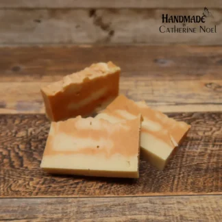 Exotic Retreat handmade Hand & Body Soap with rich golden and creamy white swirls, placed on a rustic wooden surface, created by Catherine Noel.