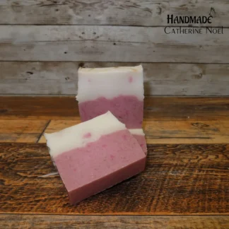 Frosted Whimsy handmade Hand & Body Soap with a pink and white layered design, placed on a rustic wooden surface, created by Catherine Noel.