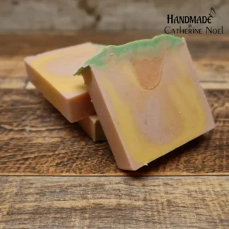 Peach Bliss handmade Hand & Body Soap with soft peach and golden yellow hues, topped with green accents, placed on a rustic wooden surface, created by Catherine Noel.