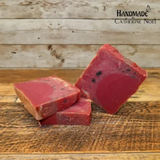 Sugared Berries handmade Hand & Body Soap with vibrant red hues and black berry-like accents, placed on a rustic wooden surface, created by Catherine Noel.