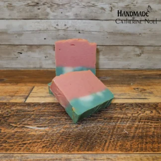 Watermelon handmade Hand & Body Soap with cheerful pink and green layers, mimicking a slice of watermelon, placed on a rustic wooden surface, created by Catherine Noel.