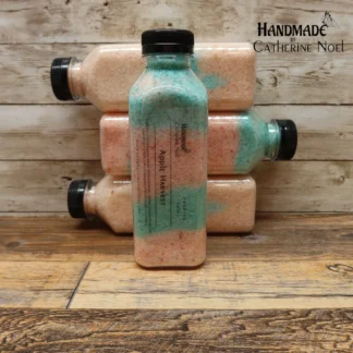 Apple Harvest soaking salts in a clear plastic bottle with orange and green tones, labeled "Handmade by Catherine Noel," displayed on a rustic wooden surface.