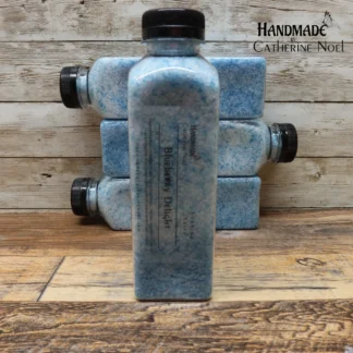 Blueberry Delight soaking salts in a clear plastic bottle with vibrant blue tones, labeled "Handmade by Catherine Noel," displayed on a rustic wooden surface