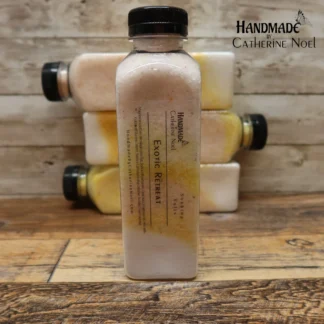 Exotic Retreat soaking salts in a clear plastic bottle with warm yellow and cream tones, labeled "Handmade by Catherine Noel," displayed on a rustic wooden background.