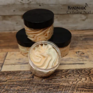 Exotic Retreat whipped body butter with golden and white creamy swirls, displayed in a clear jar with a black lid on a rustic wooden surface.