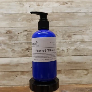 Frosted Whimsy Hand & Body Lotion in a blue bottle, set against a rustic wooden backdrop.