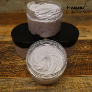 Love Bomb whipped body butter with romantic pink swirls, displayed in a clear jar with a black lid on a rustic wooden surface.
