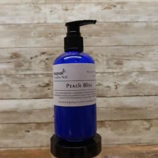 Peach Bliss Hand & Body Lotion in a blue bottle with warm peach tones, set against a rustic wooden background.