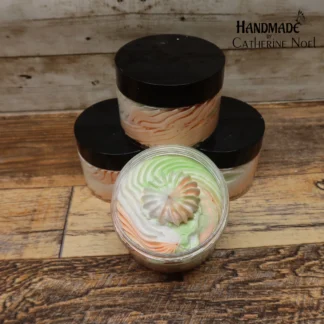 Peach Bliss whipped body butter with creamy swirls in soft peach tones, displayed in a clear jar with a black lid on a rustic wooden surface.