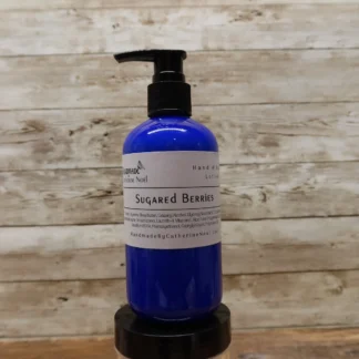 Sugared Berries Hand & Body Lotion in a blue bottle, set against a rustic wooden backdrop.