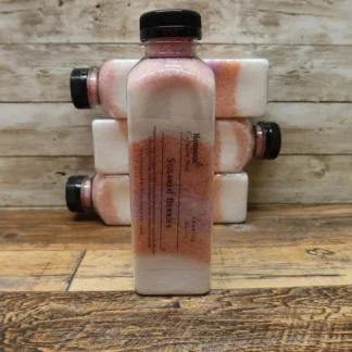 Sugared Berries soaking salts in a clear plastic bottle with layers of pink and white tones, labeled "Handmade by Catherine Noel," displayed on a rustic wooden surface.