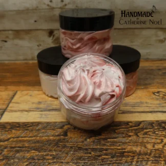 Sugared Berries whipped body butter featuring swirls of pink and white in a clear jar with a black lid, displayed on a rustic wooden surface.
