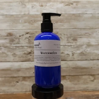 Watermelon Hand & Body Lotion in a blue bottle with playful pink and green tones, displayed against a rustic wooden background.