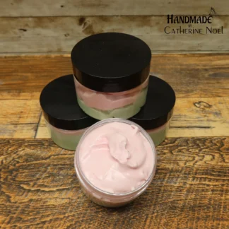 Watermelon whipped body butter with pink and green layers in a clear jar with a black lid, displayed on a rustic wooden surface.