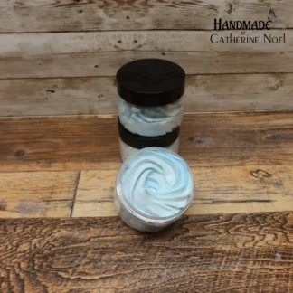 Winter Frost whipped body butter with cool blue swirls in a clear jar with a black lid, displayed on a rustic wooden surface.